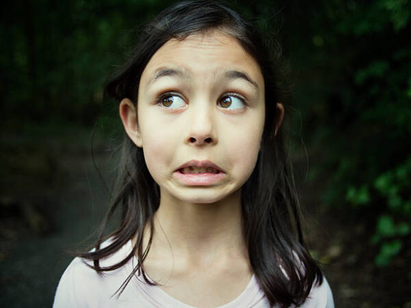 Mädchen mit dunklen Haaren, das verängstigt nach links schaut und den Mund verzieht.